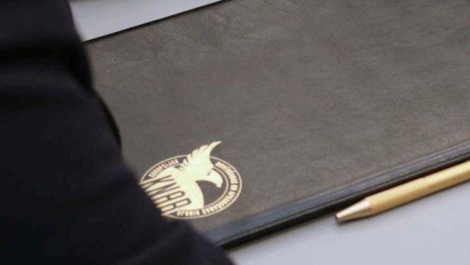 Attēlā redzama mape ar KNAB logo